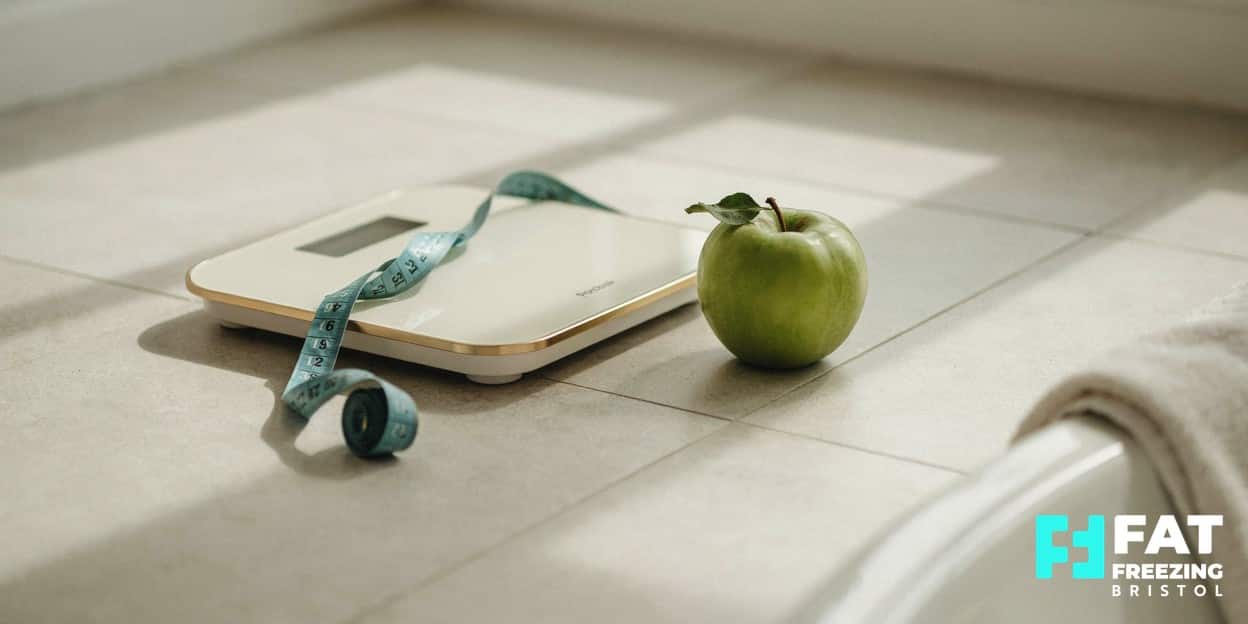 Still-life of a blank bathroom scale with a measuring tape draped across it and a green apple beside it, contrasting weight with the body contouring focus of fat freezing