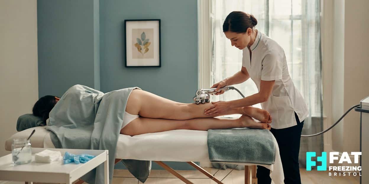 An aesthetic practitioner gliding a motorised vacuum-roller handpiece along a relaxed client’s thigh in a bright treatment room, illustrating how vacuum roller therapy differs from fat freezing