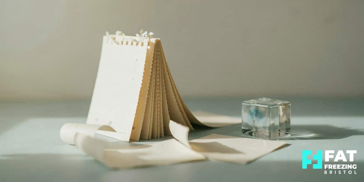 A tear-off calendar with peeling pages beside a frosted glass cube in cool light, evoking how fat freezing results last over many years