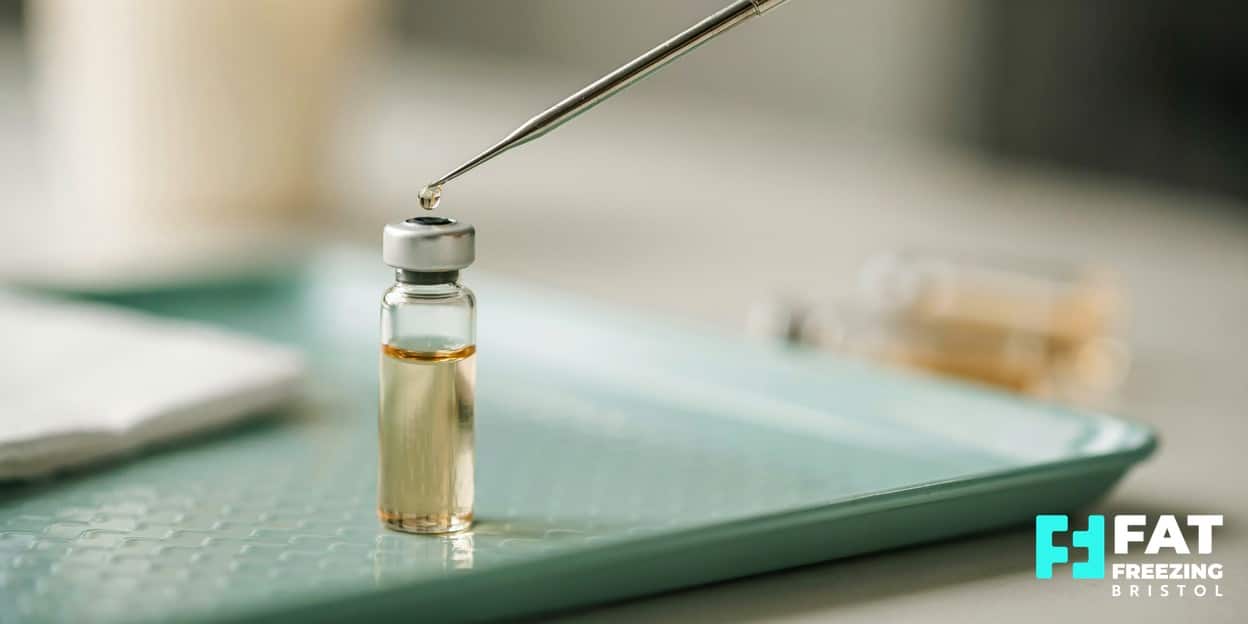 A close-up of a clear fat-dissolving treatment vial with a golden droplet at the needle tip on a mint clinic tray, representing Aqualyx’s localised approach versus Mounjaro’s systemic effect