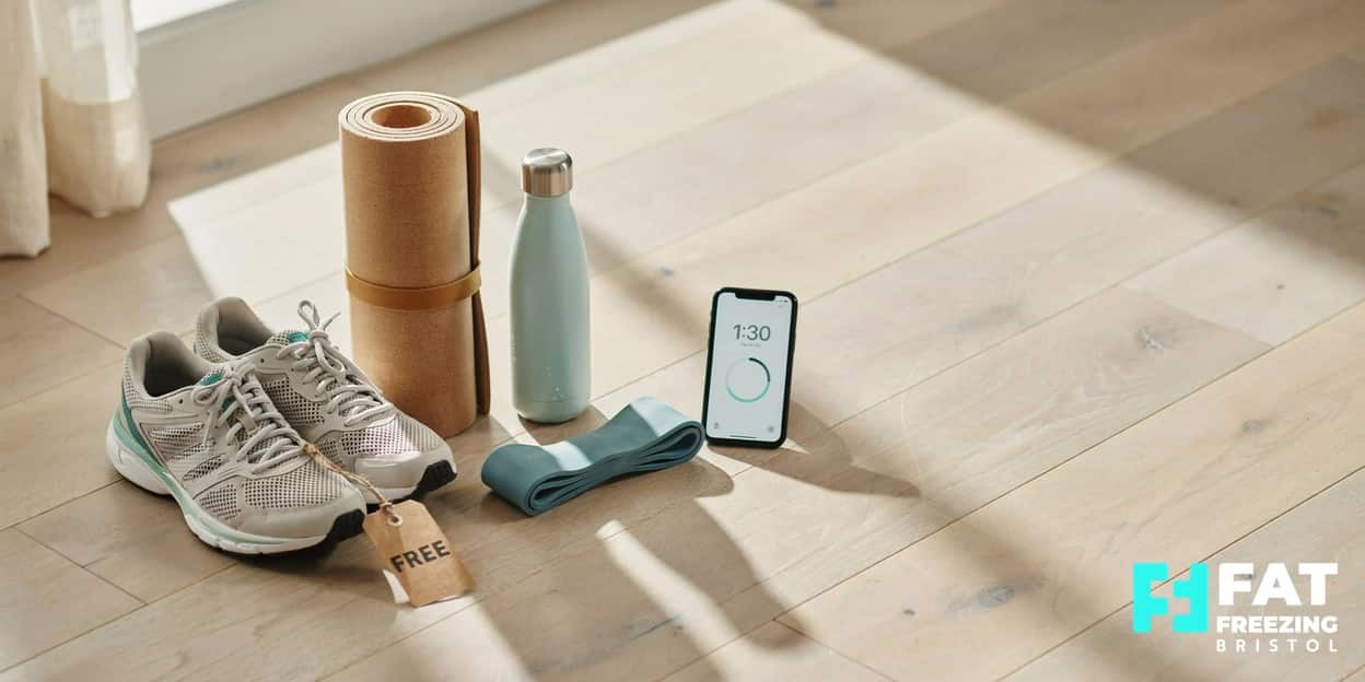 Affordable home-fitness kit including running trainers, a yoga mat, water bottle and resistance band laid out with a small tag reading FREE in soft morning daylight