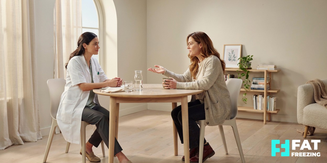 A friendly clinician and a client talking together across a table in a calm, modern consultation room with soft daylight