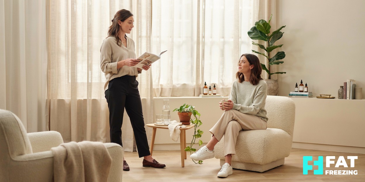 A practitioner in a calm modern clinic explaining a body-contouring treatment to a relaxed seated client