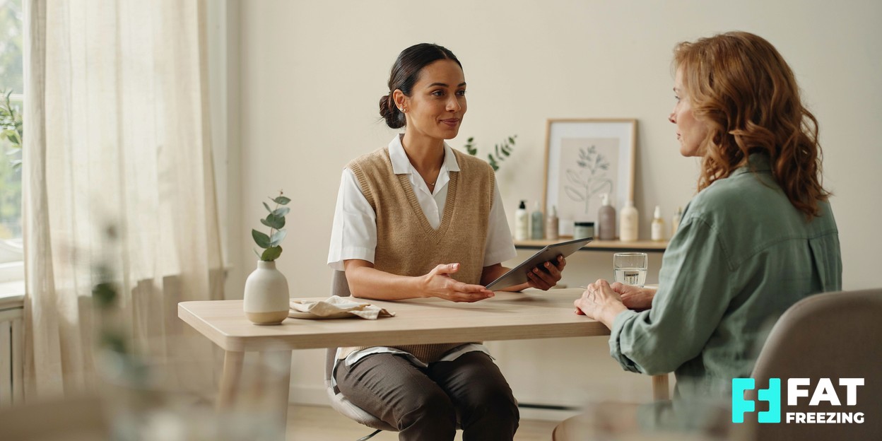 A practitioner and client talking through body-contouring options across a consultation desk in a bright, modern clinic