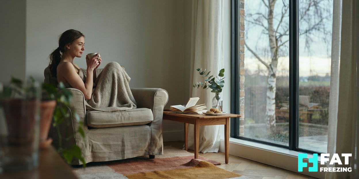 A calm person sitting thoughtfully by a window with a cup of tea in a softly lit home, weighing a personal decision