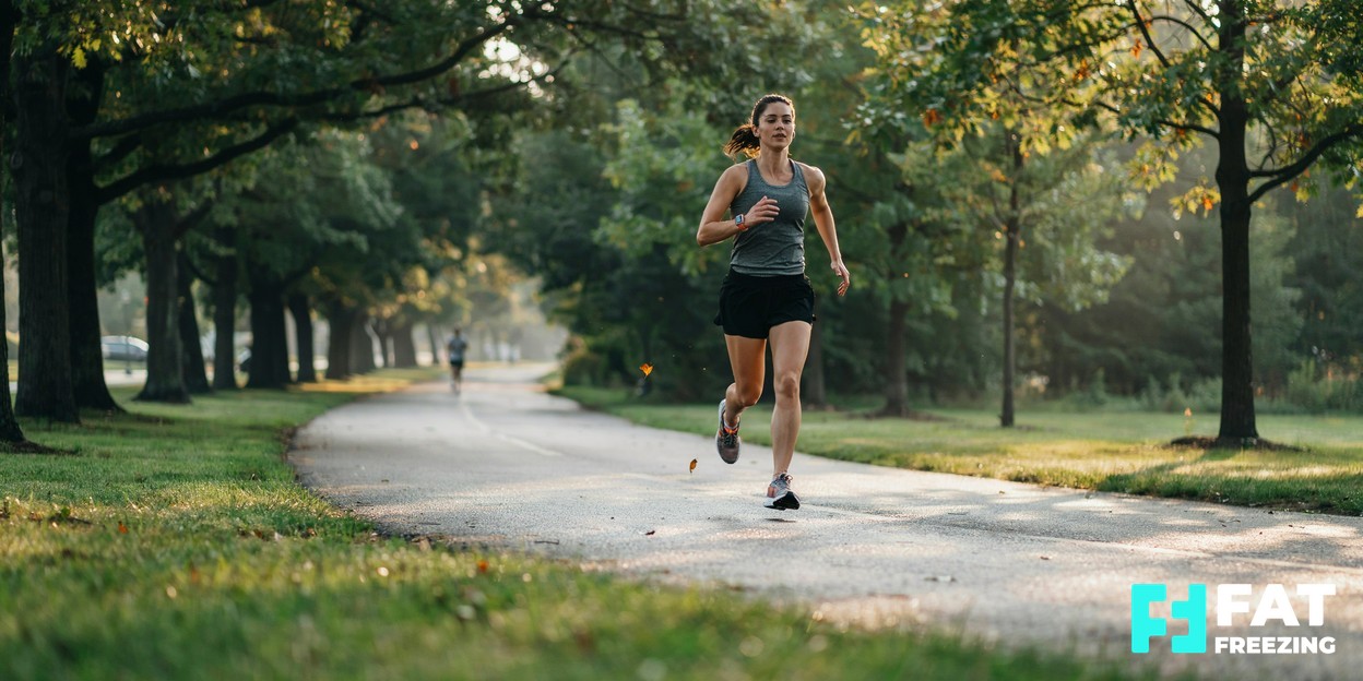 A woman jogging along a tree-lined path in soft early morning light, embodying an active, healthy lifestyle